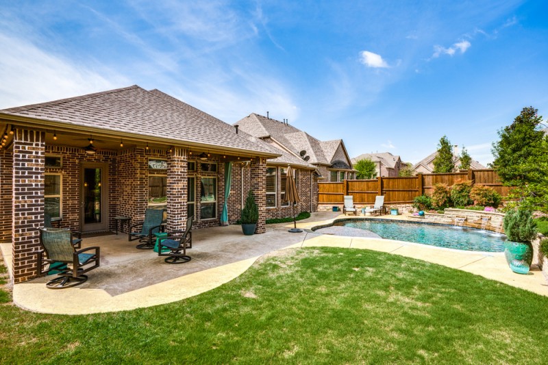    Serene Grassy Backyard with Covered Patio and Sparkling Swimming Pool 